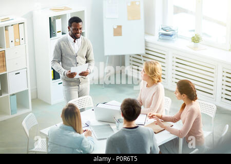Handsome African American manager with toothy smile presenting his creative ideas to colleagues while having working meeting at spacious boardroom Stock Photo