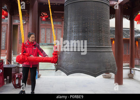 Nanjing, Jiangsu, China.  Young Woman Ringing the Bell in the Bell Pavilion of the Confucian Temple Complex. Stock Photo