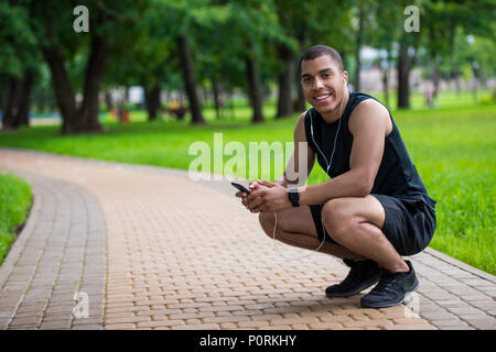 smiling young african american sportsman using smartphone while crouching in park Stock Photo