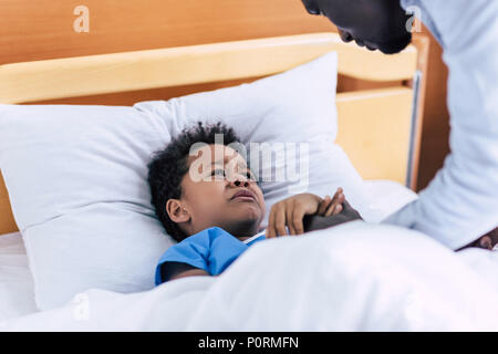 selective focus of crying african american boy lying in bed and looking at father in hospital Stock Photo