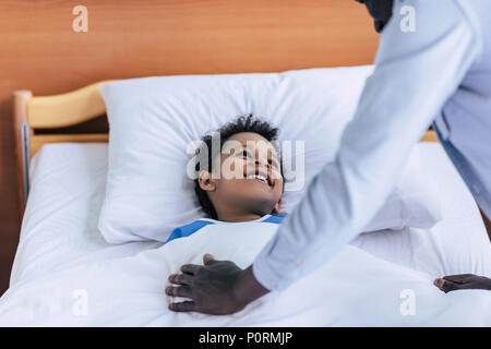 happy african american boy looking at father while lying in bed in clinic Stock Photo