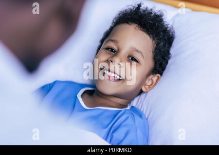 selective focus of cheerful african american little boy looking at camera while lying in bed Stock Photo