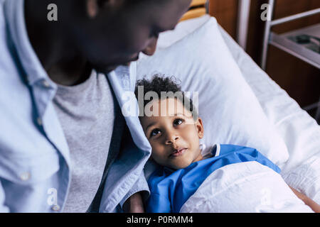 happy african american boy looking at father while lying in bed in clinic Stock Photo