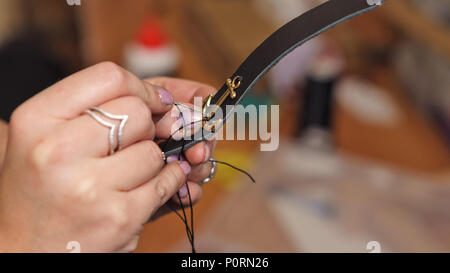Tanner sews decorative part of anchor to leather bracelet with needle and threads. Process works in studio close-up. Stock Photo