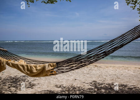 A towel in an empty hammock, swinging over the sand on a tropical beach, close to the sea, Gili Trawngan, Indonesia, April 25, 2018 Stock Photo