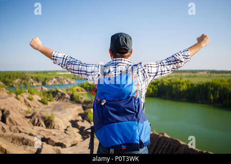 Picture from back of young tourist with backpack with hands up against background of mountain landscape, lake Stock Photo