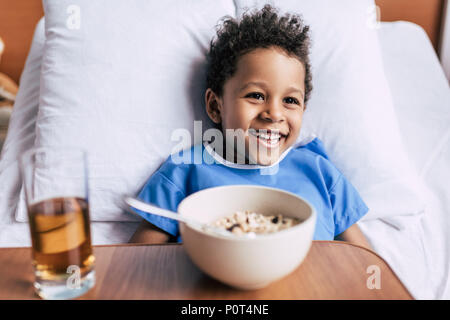portrait of cheerful african american boy with breakfast in bed in clinic Stock Photo
