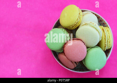 Colorful macaroons in bowl on vivid pink surface with copy space Stock Photo