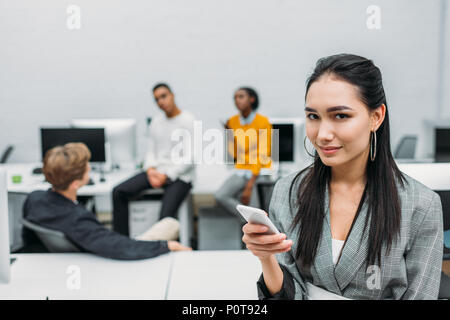 young asian businesswoman using smartphone with blurred partners on background Stock Photo