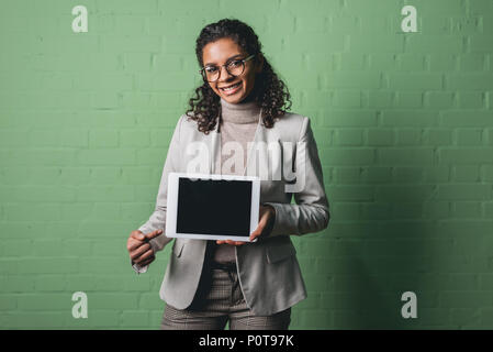 young african american businesswoman presenting digital tablet in front of green wall Stock Photo