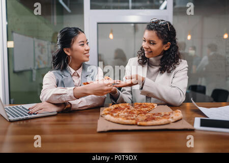 black and asian businesswomen eating pizza and working in office Stock Photo