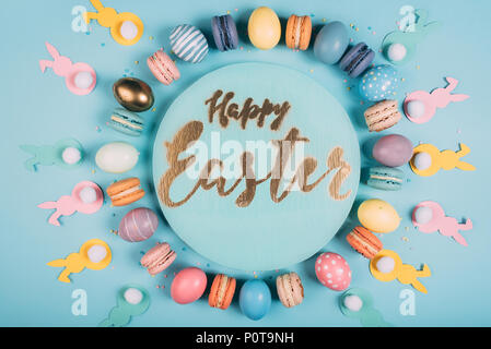 top view of round board with happy easter lettering and colorful easter decor around on blue surface Stock Photo