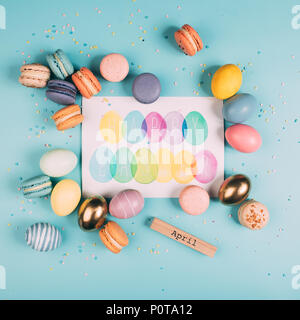top view of easter eggs and macarons around happy easter greeting card on blue surface Stock Photo