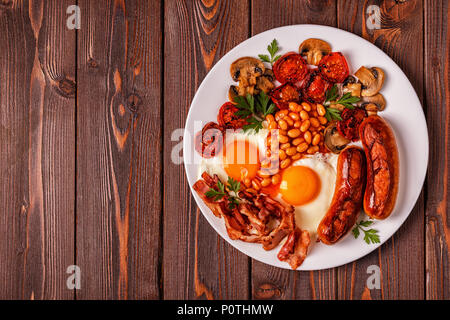 Traditional full English breakfast with fried eggs, sausages, beans, mushrooms, grilled tomatoes and bacon on wooden background. Top view Stock Photo