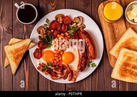 Traditional full English breakfast with fried eggs, sausages, beans, mushrooms, grilled tomatoes and bacon on wooden background. Top view Stock Photo