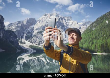 Smiling young man (tourist) taking selfie against Lake Braies and mountains range of Alps  - Dolomites, Italy Stock Photo