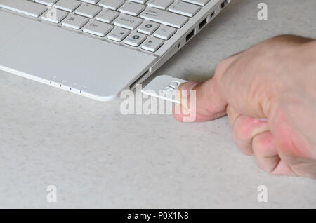 A male hand inserts a white compact SD card into the corresponding input in the side of the white netbook. Man uses modern technologies to store memor Stock Photo