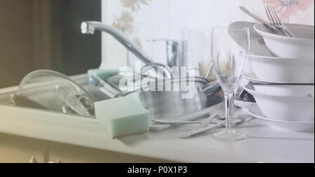 A huge pile of unwashed dishes in the kitchen sink and on the countertop. A lot of utensils and kitchen appliances before washing. The concept of dail Stock Photo