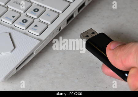 A male hand inserts a black compact USB card into the corresponding input in the side of the white netbook. Man uses modern technologies to store memo Stock Photo
