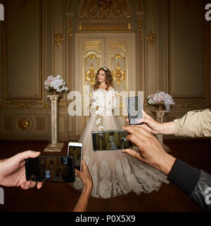 Guests take photographs of the bride on smartphones. Focus on smartphones. Stock Photo