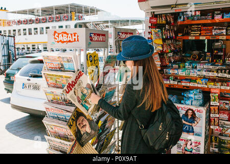 Istanbul, June 17, 2017: Young beautiful girl in a hat with a backpack buys a magazine or newspaper in a street press store Stock Photo