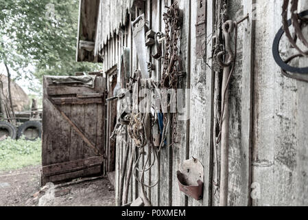 Old stables, on the wall hanging various tools and horse harness, at an angle. Stories about rural life in Ukraine Stock Photo