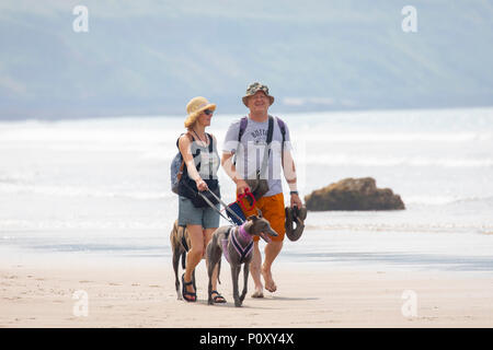 A couple walking their dog along the sany beach at Whitsand Bay in Cornwall dressed for the hot summer weather wearing sun hats, Cornwall, UK Stock Photo