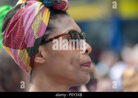 Edinburgh, Scotland, UK. 10th June, 2018. A woman wearing a colourful head scarf and sunglasses during the Edinburgh Processions Artwork march celebrating 100 years since British women won the right to vote. Thousands of women came together in the four capitals of the UK,  Belfast, Cardiff, Edinburgh and London. The Participants wore either a green, white or violet scarf and walked in stripes through the city streets to depict the colours of the suffragettes. Credit: Skully/Alamy Live News Stock Photo