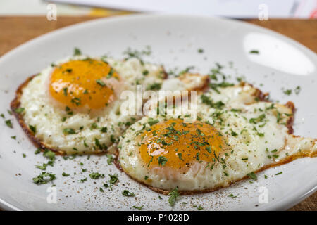 Two Fried Eggs On The White Plate With Salt, Black Pepper and Green Parsley Stock Photo