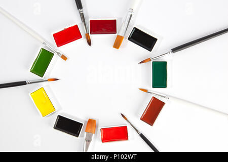 Solid watercolors pans with various paint brushes arranged in circle with copy space on white background Stock Photo