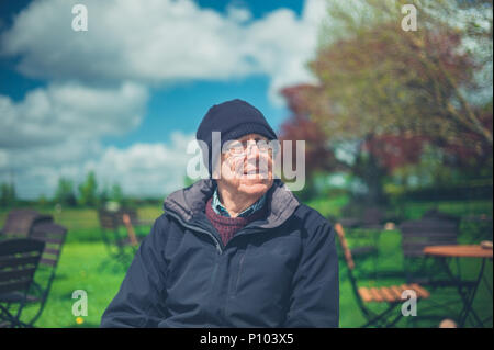 A senior man is sitting outside in a garden on a sunny day Stock Photo