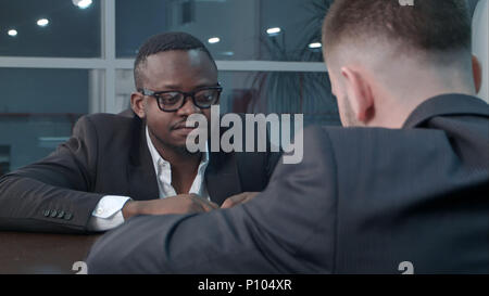 Pensive afro-american and caucasian businessmen working through papers and discussing financial report having concentrated looks, sitting close to each other Stock Photo