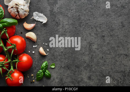 Food background. Flat lay of fresh tomatoes with basil, garlic and sea salt on black stone background. Top view with copy space. Stock Photo