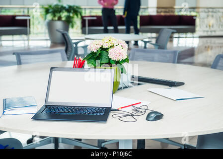Modern stylish work place with laptop with blank white screen, notebook, stationery and flower pot on the desk at open space office. Minimalism busine Stock Photo
