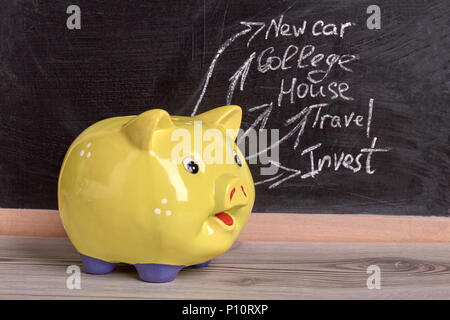 Savings in yellow moneybox. Collectiong money for new car, college, house, travel and invest. Black board background. Stock Photo