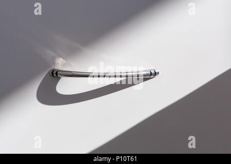 Closeup of modern stainless drawer handle with long shadow in ray of sunlight Stock Photo