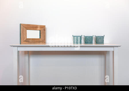 Empty picture frame with three decorative candle holders on white side table against white wall with copy space Stock Photo