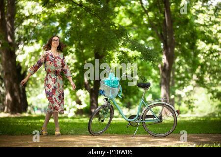 girl standing infornt of vintage bicycle on a road in the park Stock Photo