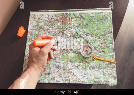 Man holding an orange marker above a map looking for a path Stock Photo