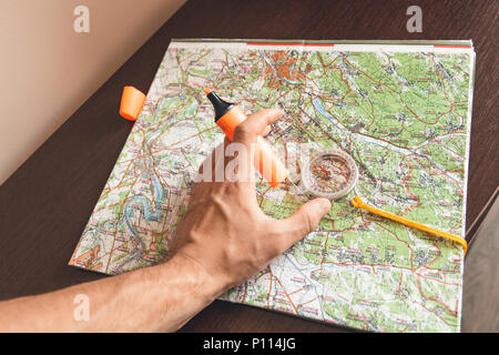 Man holding an orange marker above a map looking for a path Stock Photo