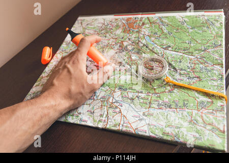 Man holding an orange marker above a map looking for a path Stock Photo