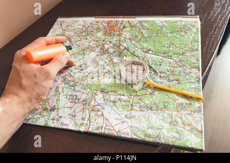Man holding an orange marker above a map looking for a path Stock Photo