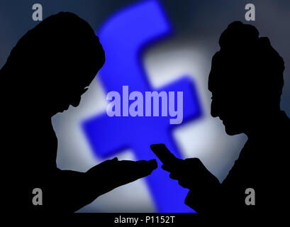 Silhouettes of a couple of people using the Facebook app on smartphones. Stock Photo