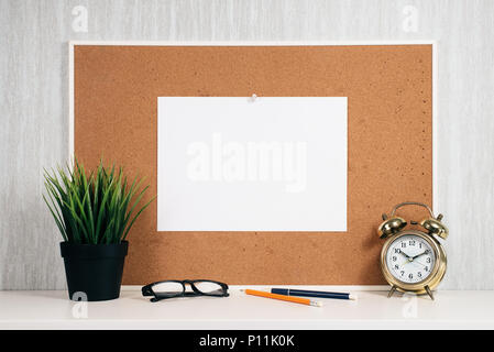 Blank paper note on cork board with golden alarm clock, reading glasses, pen and green plant in pot. memo and time management concept. blank note for  Stock Photo