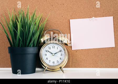 Blank paper note on cork board with golden alarm clock and green plant in pot. memo and time management concept. blank note for copy space or typograp Stock Photo