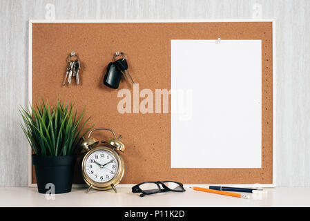 Blank paper note on cork board with car key, golden alarm clock, reading glasses, pen and green plant in pot. memo and time management concept. blank  Stock Photo