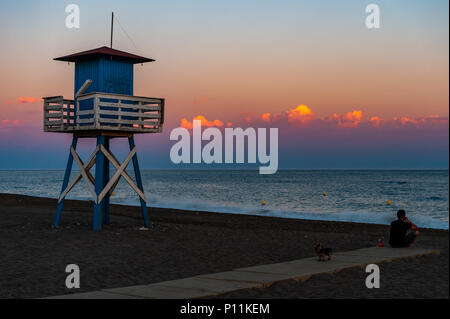 Man and his dog on the beach next to a lifeguard tower at sunset in Axarquía, la Cala del Moral municipality of Rincón de la Victoria, Malaga, Spain. Stock Photo