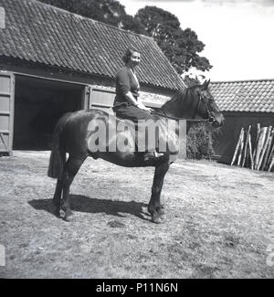 1951, historical, young lady sitting on a horse in a farmyard, England, UK. Stock Photo