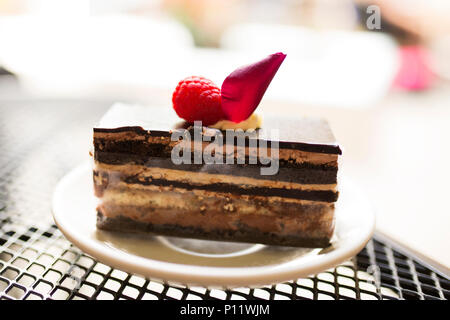 A slice of chocolate opera cake garnished with strawberries on a white plate, on a metal table at an outdoor cafe in New Orleans, Louisiana. Stock Photo