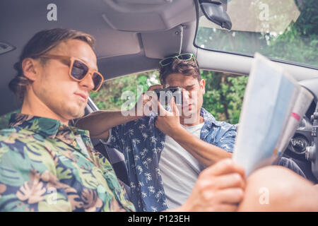Hipsters sitting in car and taking vacation photos and holding map. On the road journey concept. Stock Photo